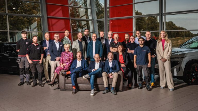 Groepsfoto van een team in een showroom met twee auto's op de achtergrond