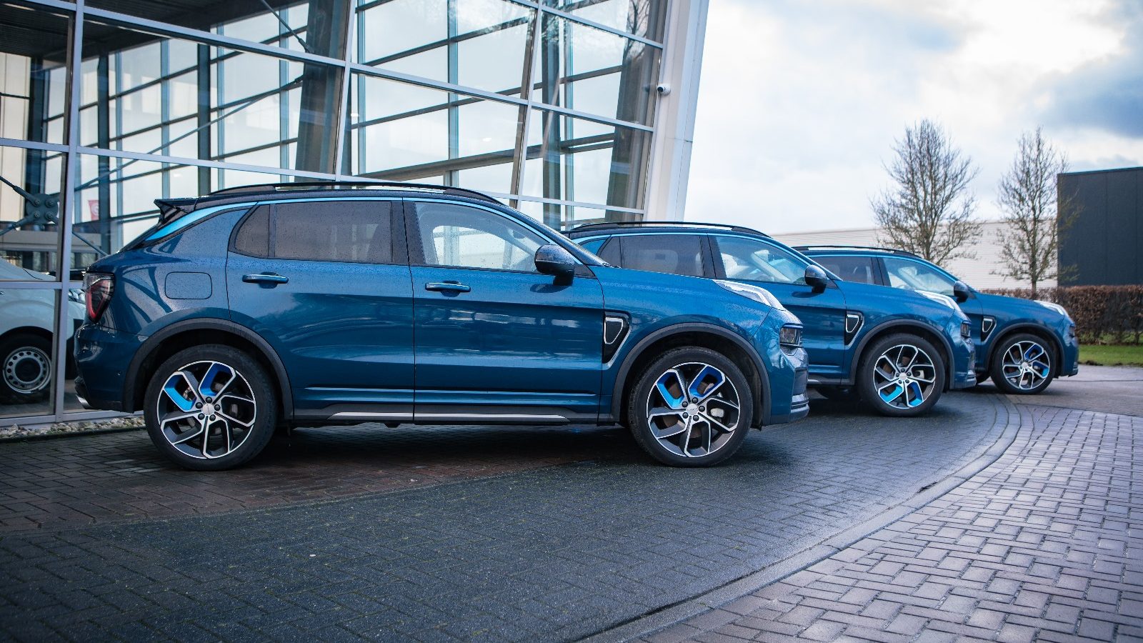 Drie blauwe SUV’s geparkeerd naast een glazen gebouw