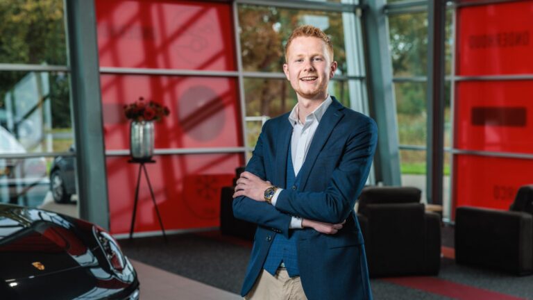 Jonge man in pak met gekruiste armen staat lachend in een moderne showroom