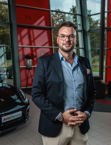 Man met bril in pak poseert in showroom naast zwarte auto