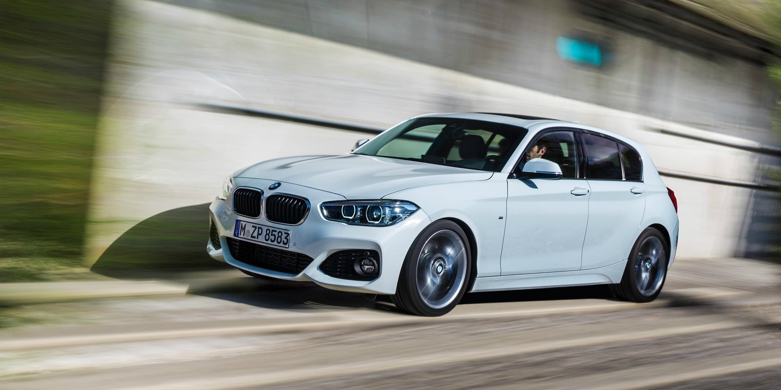 Witte BMW hatchback rijdt met bewegingsonscherpte langs een betonnen muur
