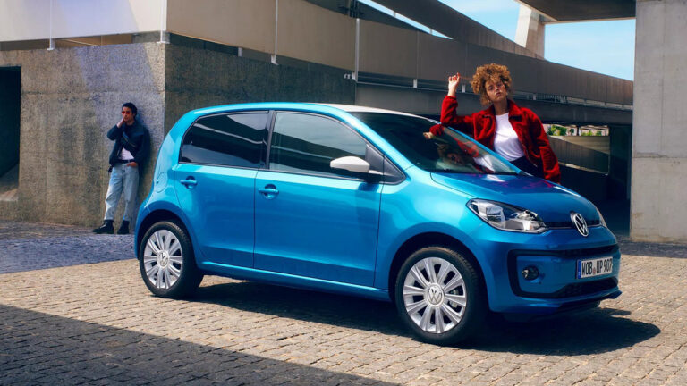 Blauwe Volkswagen Up geparkeerd onder een viaduct, met twee personen ernaast
