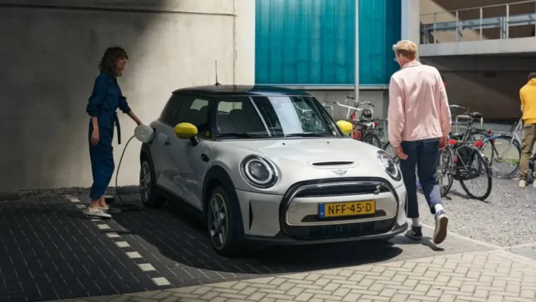 Witte Mini Cooper SE aan laadpaal, met twee mensen ernaast op een binnenplaats