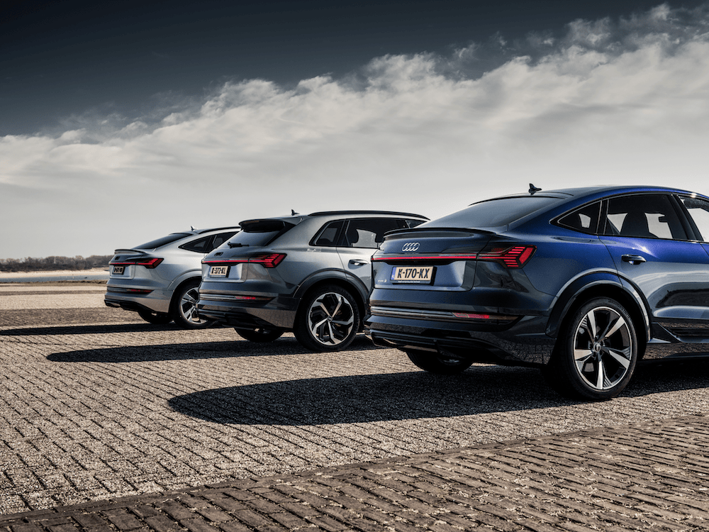 Drie Audi SUV-coupés van achteren geparkeerd op een open bestrate vlakte onder een bewolkte lucht