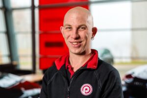 Portret van een glimlachende kale man in zwart-rode werkkleding binnenshuis