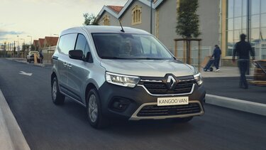 Witte Renault Kangoo bestelwagen rijdt op een straat langs gebouwen