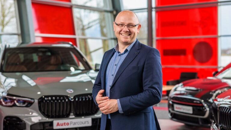 Lachende man in pak in showroom tussen twee auto's