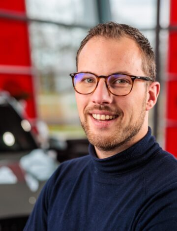 Man met bril en donkerblauwe trui glimlacht naar de camera