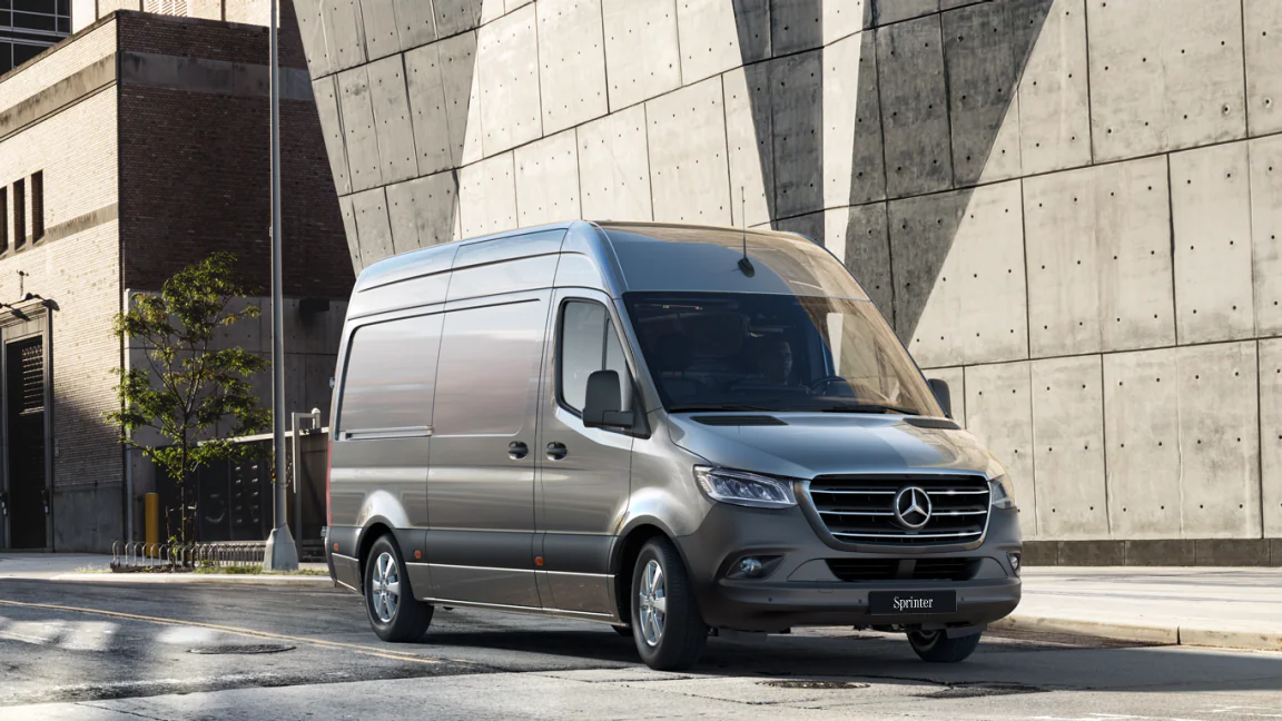 Zilverkleurige Mercedes-Benz Sprinter bestelbus geparkeerd aan een straat bij een betonnen gevel