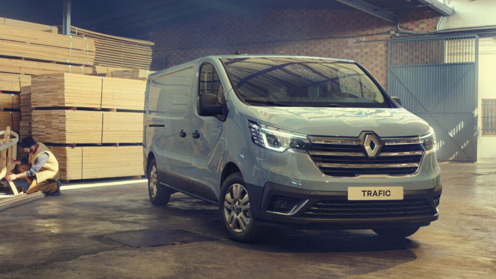 zilvergrijze Renault Trafic bestelwagen in een loods naast stapels hout en een knielende man